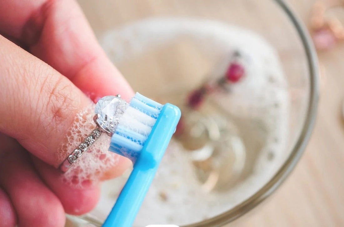 Soft toothbrush cleaning a lab grown diamond engagement ring in warm water