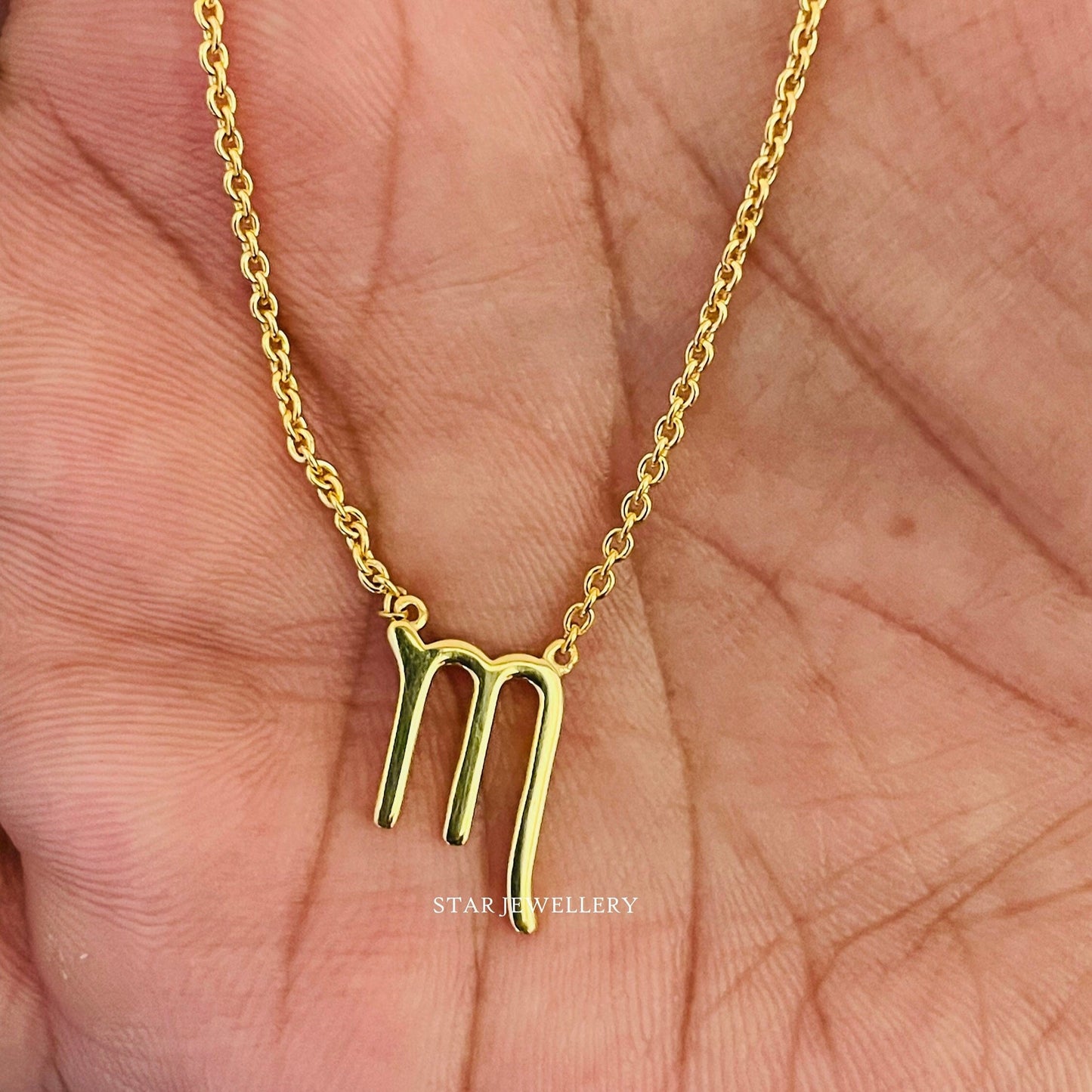 A gold necklace with a Scorpio zodiac sign charm held in a person's hand.